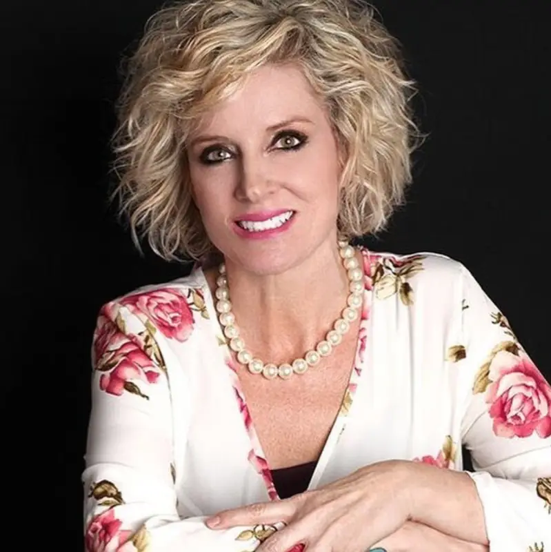 Donna Starnes in a floral blazer and pearls, studio portrait on black